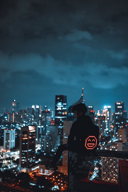 Man with Backpack Sitting on Rooftop of Skyscraper · Free Stock Photo