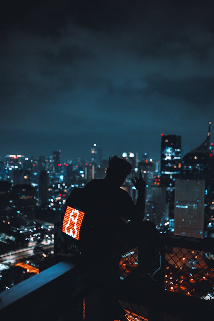 Man Sitting On Wall In City At Night