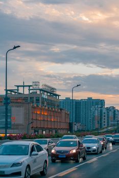 Cars in city traffic with urban backdrop and cloudy sunset sky