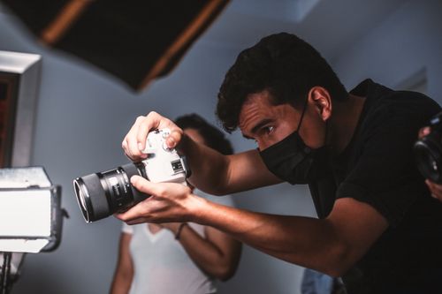 Free Photographer wearing mask focused on capturing image indoors. Stock Photo