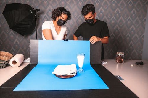 Photo of Two People in Face Masks Preparing a Composition for a Photoshoot in a Studio