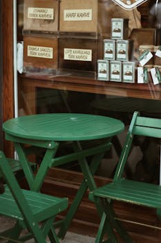 Charming café setup with green chairs and table, perfect for a relaxing day outdoors.