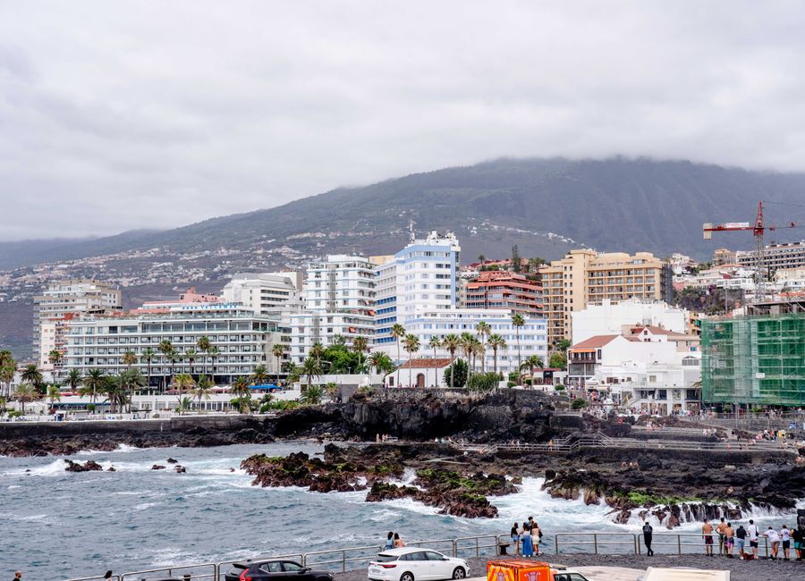 Seaside cityscape of Puerto de la Cruz, Tenerife, featuring hotels, rocky shore, and cloudy sky.