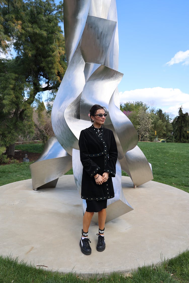 Stylish Woman Standing Near Modern Sculpture In Park