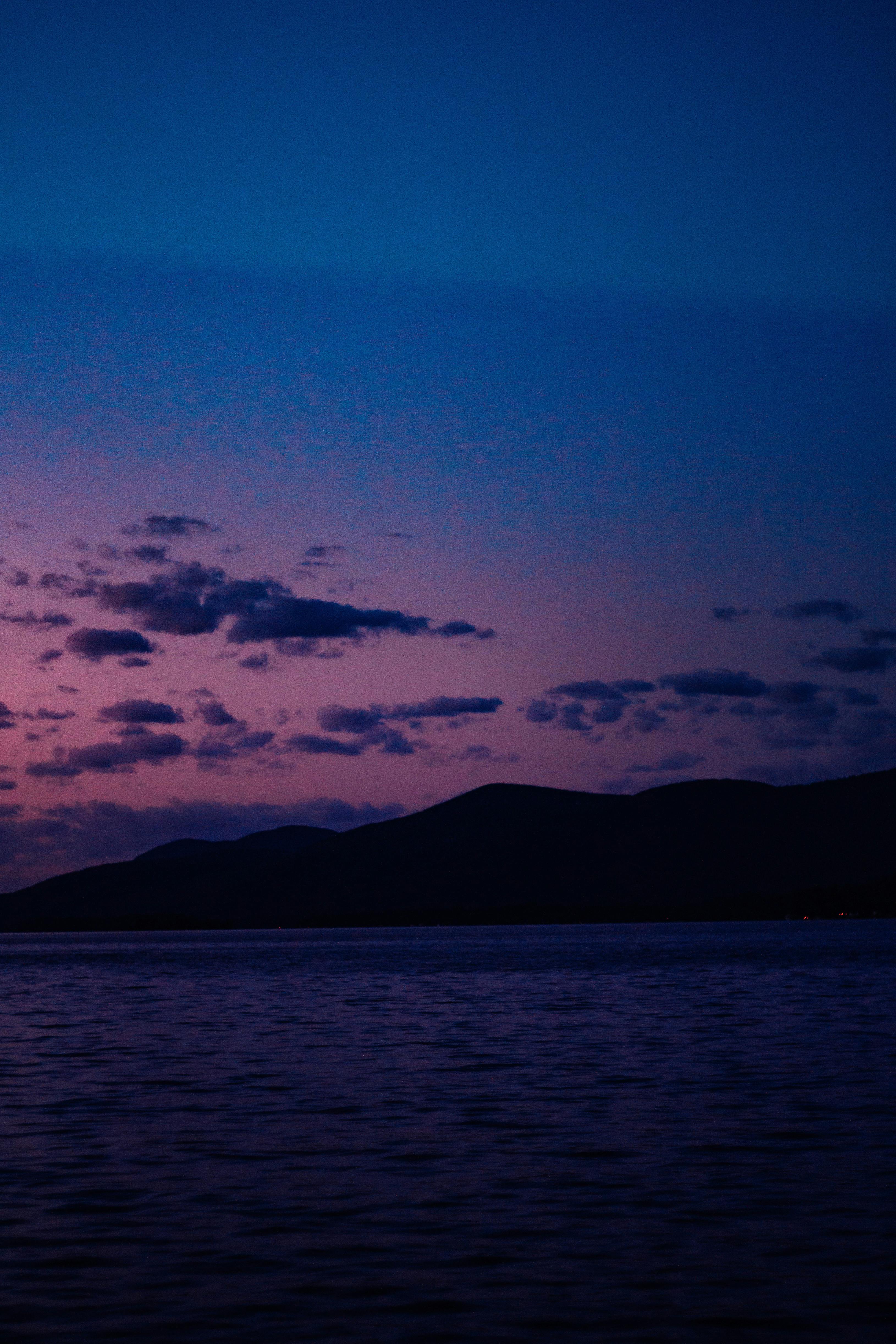 A calm sea meets silhouetted mountains under a dramatic twilight sky.