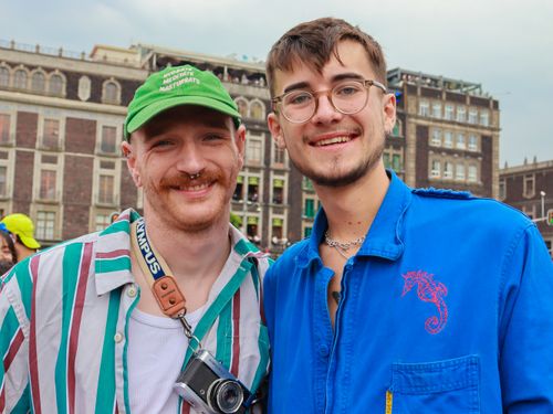 Free Two young men smiling at the camera, enjoying an outdoor gathering in front of historic buildings. Stock Photo