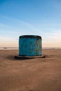 A solitary blue barrel on a serene beach at sunset, showcasing textures and colors.