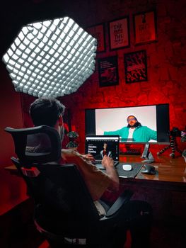 Man working in a moody lit studio with laptop and monitor featuring digital content.