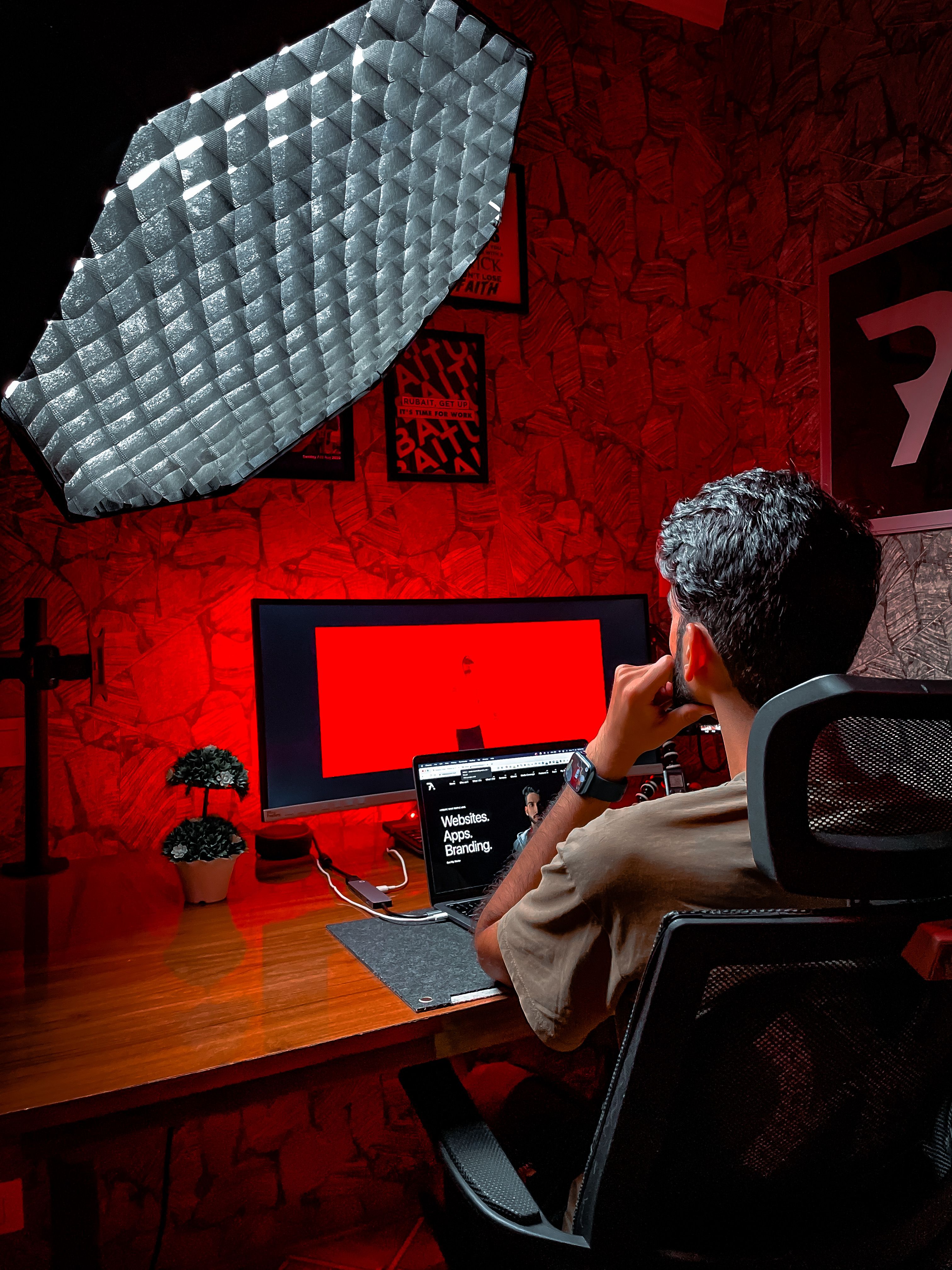 A freelancer working on a laptop in a dimly lit studio with red ambient lighting, focusing on coding.