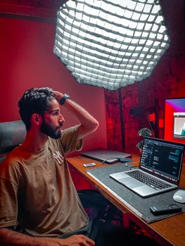 A programmer working late at night with a laptop in a dimly lit studio setting.