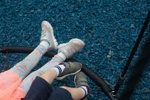 Two children enjoying a swing at a playground with blue rubber mulch.