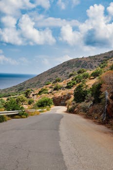 Explore the picturesque coastal road in Crete with stunning mountain and sea views under a cloudy sky.