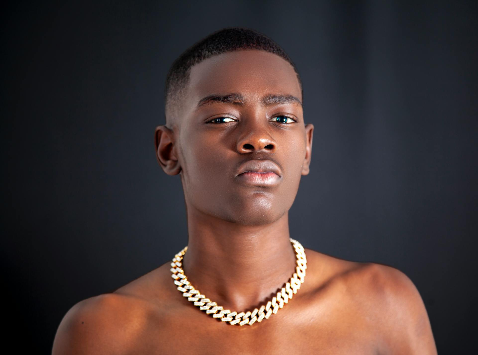 Close-up portrait of an African American teenager wearing a gold necklace against a dark background.