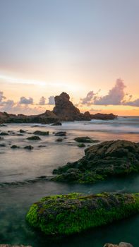 Vivid sunset over rocky coastal formations with waves and mossy rocks.