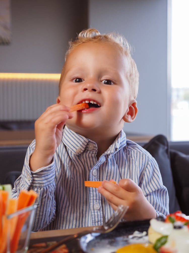 Close-Up Shot Of A Little Boy Eating Sliced Carrots