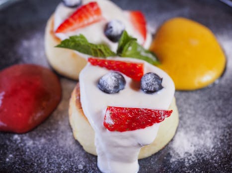 Close-up of pancakes with strawberries, blueberries, and cream, garnished with mint leaves.