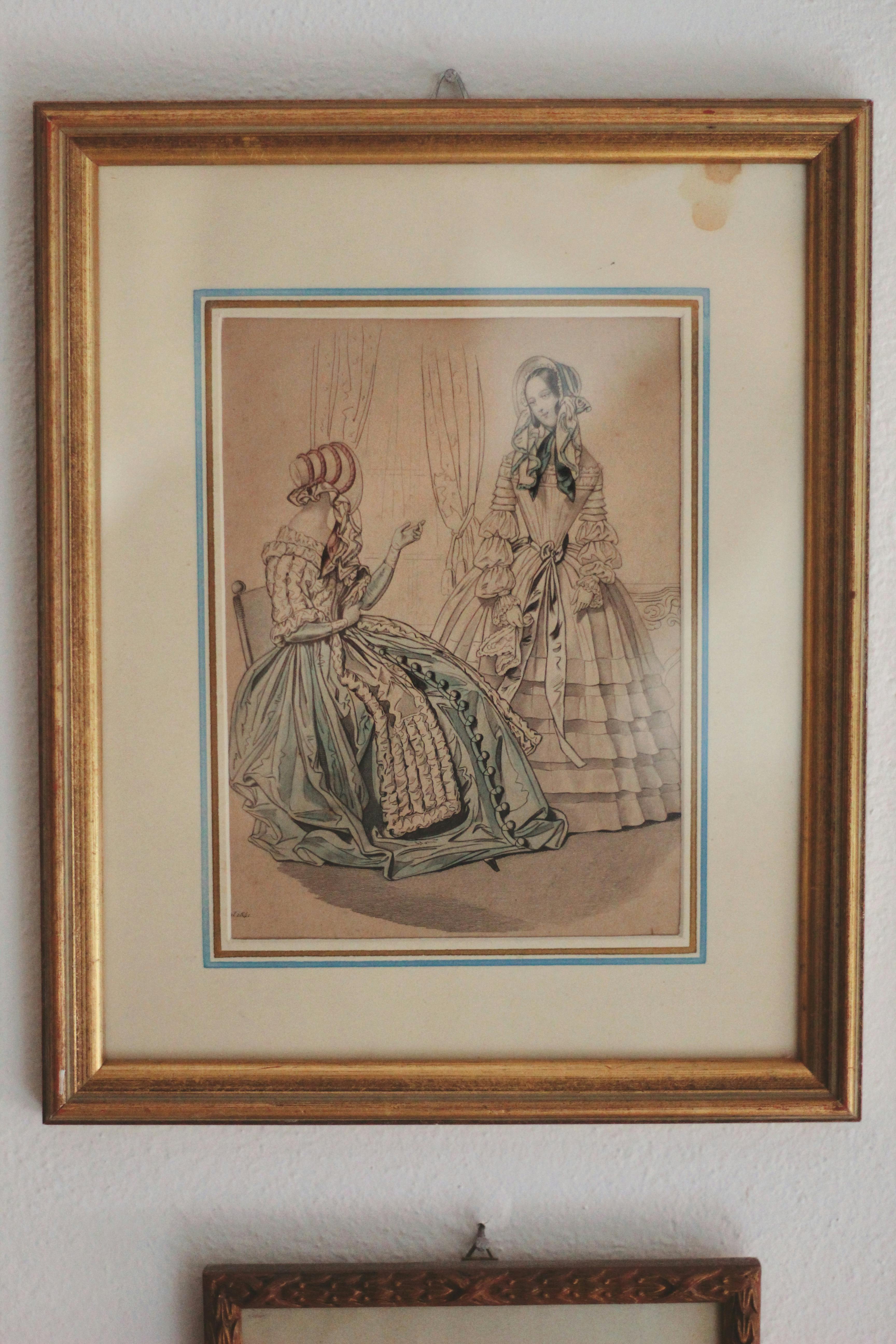 Antique framed illustration depicting two women in Victorian attire, showcasing period fashion and decor.