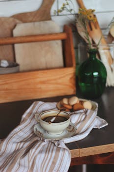 A warm, inviting coffee setup with a ceramic cup, macarons, and rustic kitchen decor.