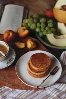 Elegant breakfast setting with pancakes, fruit, coffee, and an open book.