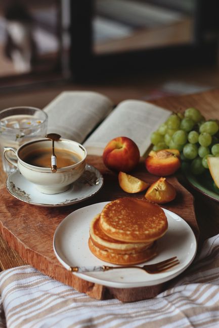 Inviting breakfast scene with pancakes, coffee, grapes, and peaches on a wooden table.