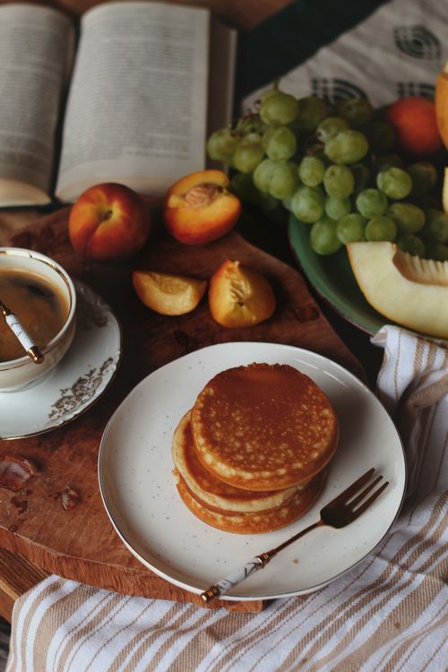 Free A cozy morning setup with pancakes, coffee, and fresh fruits like peaches and grapes on a wooden table. Stock Photo