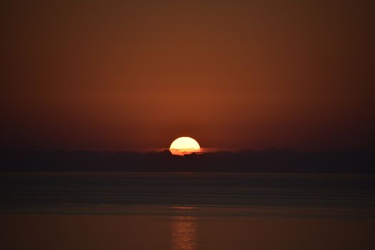 A serene sunset over the ocean with the sun setting below the horizon and reflecting on the water surface.
