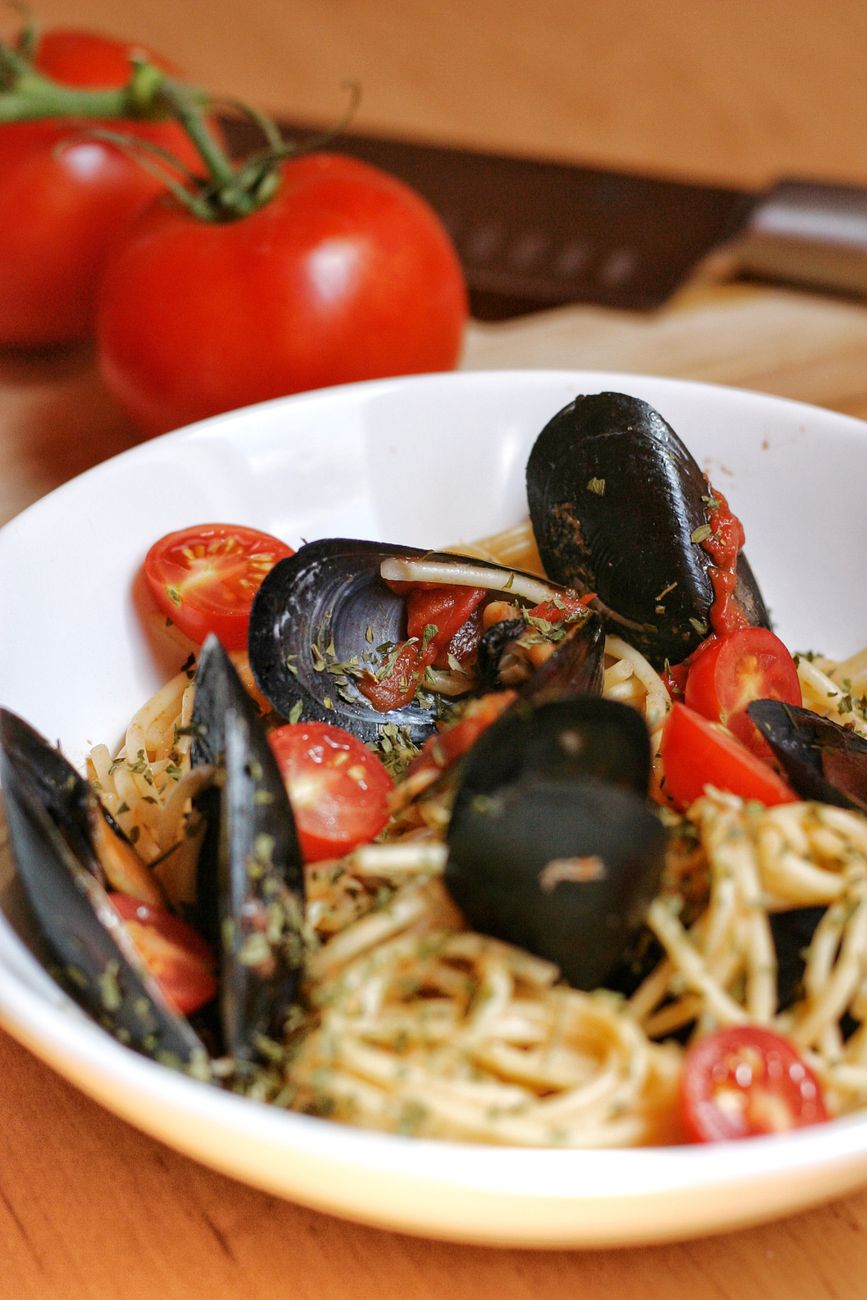 A generous bowl of spaghetti all'arrabbiata with mussels, the pasta glistening with spicy red tomato sauce, opened mussels nestled throughout, finished with bright green parsley and a sprinkle of grated cheese