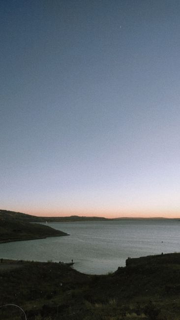 Fotomural Captura la tranquilidad del ocaso sobre un océano expansivo con colinas distantes en silueta contra un cielo crepuscular.