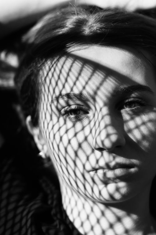 Free Artistic black and white portrait of a woman with intricate shadow patterns across her face. Stock Photo