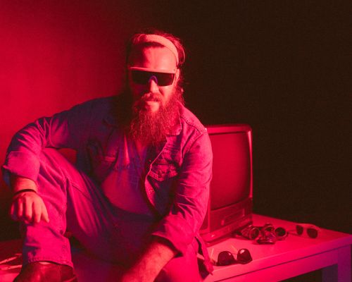 Free Stylish bearded man wearing sunglasses seated beside a vintage TV under red lighting. Stock Photo