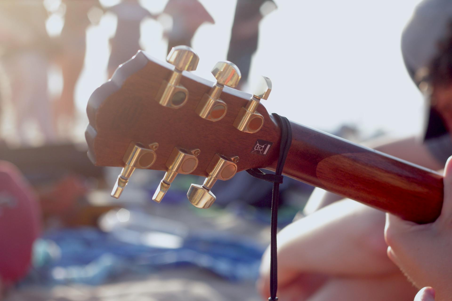 Guitar headstock with tuning pegs in focus at a sunny outdoor gathering.