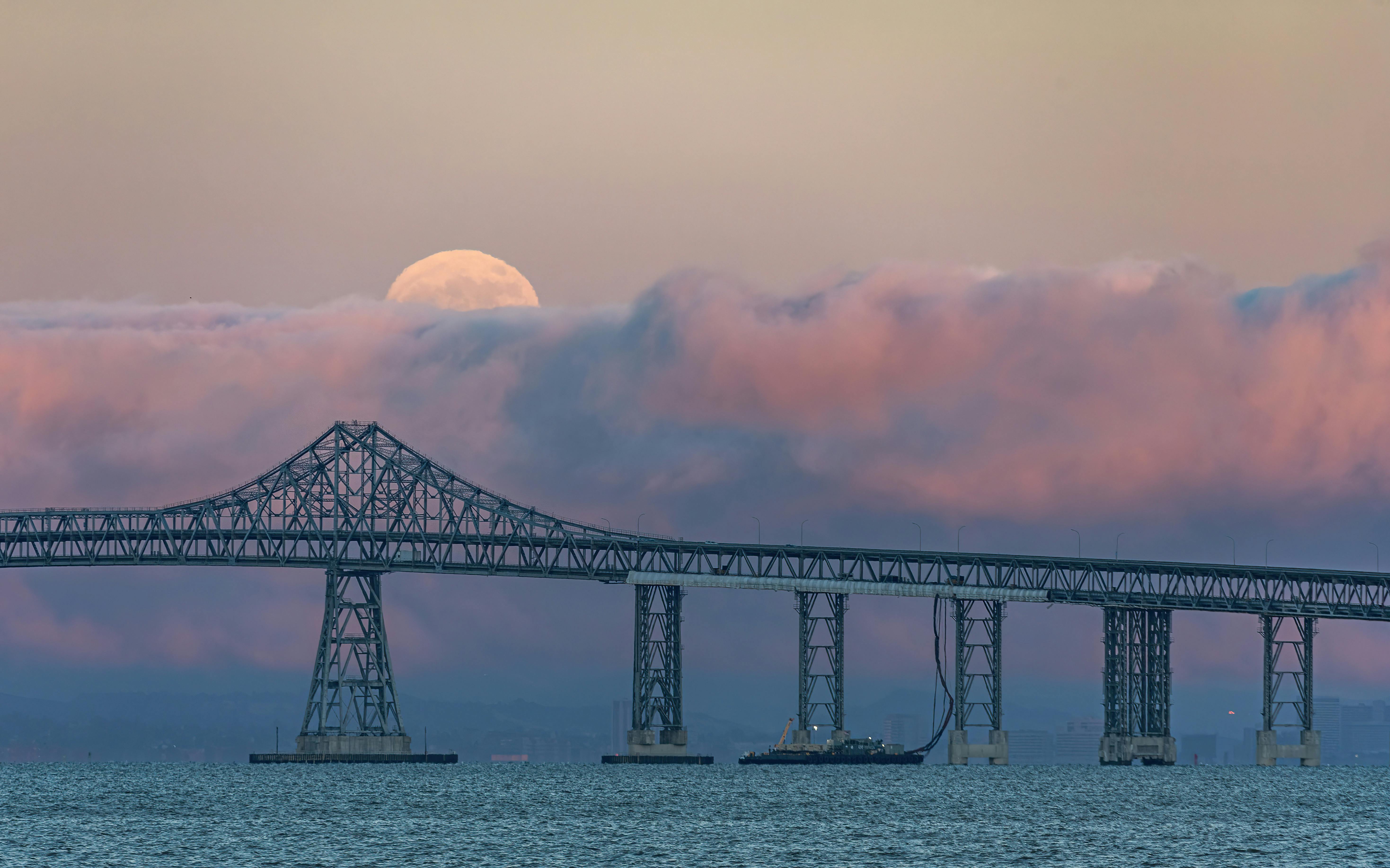 dusk over the richmond san rafael bridge with a super moon peeking above purple clouds