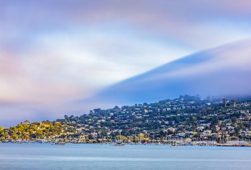 Free Stunning view of a tranquil harbor town with anchored boats and hillside homes at dawn. Stock Photo