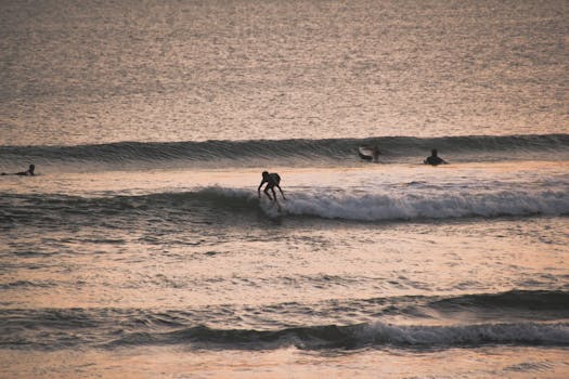A surfer rides the waves during a stunning sunset on a Bali beach, showcasing water sports excitement.