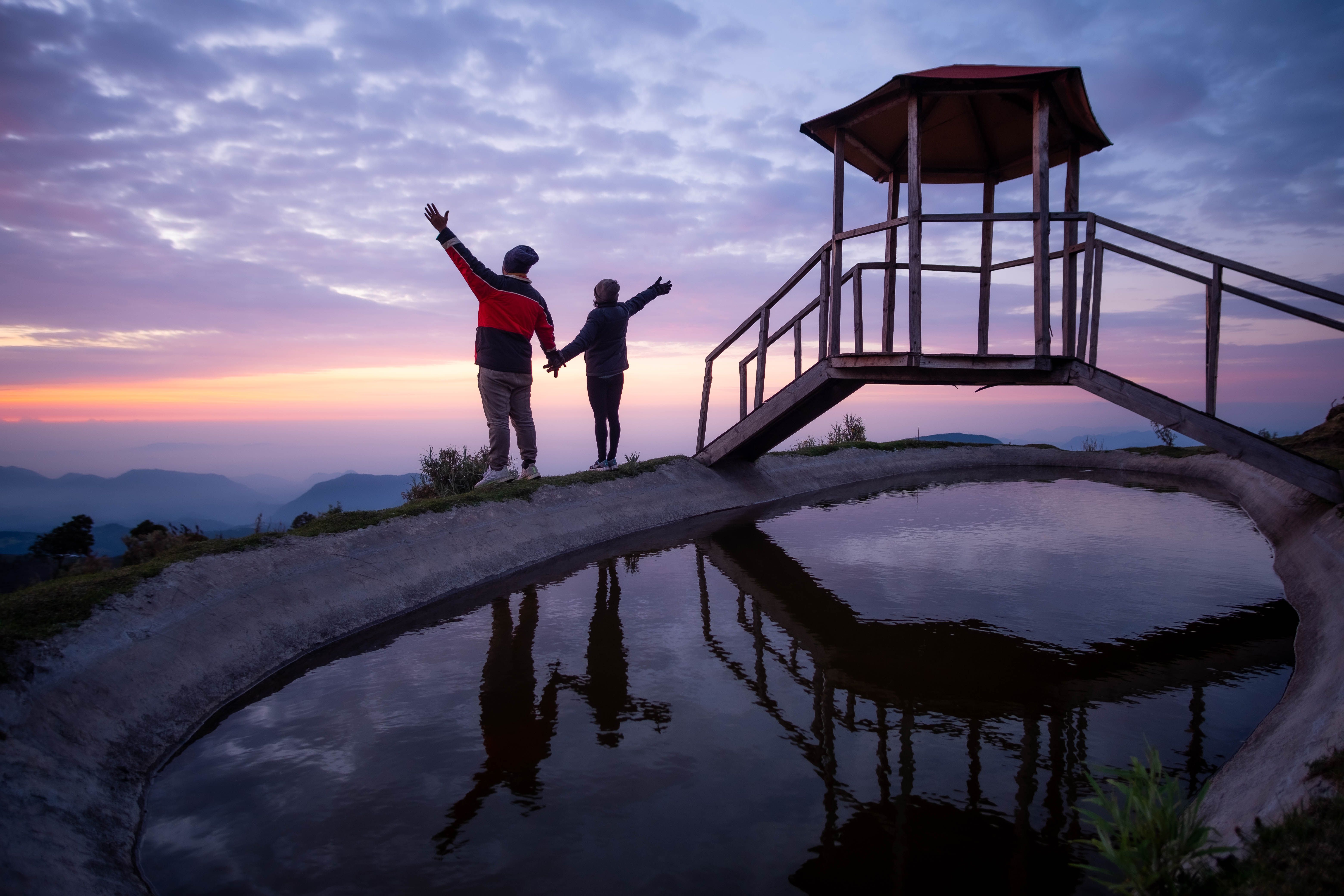 Two people silhouetted beside water at sunset in the mountains