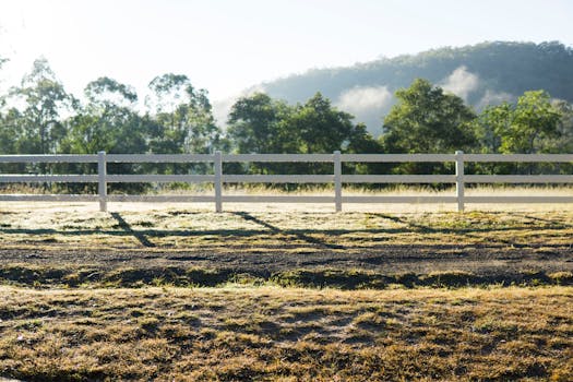 Peaceful morning view of rural landscape in Ghan, Australia with white fence and hills.
