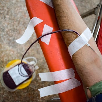 Detailed view of arm during blood donation, highlighting needle insertion and blood bag.