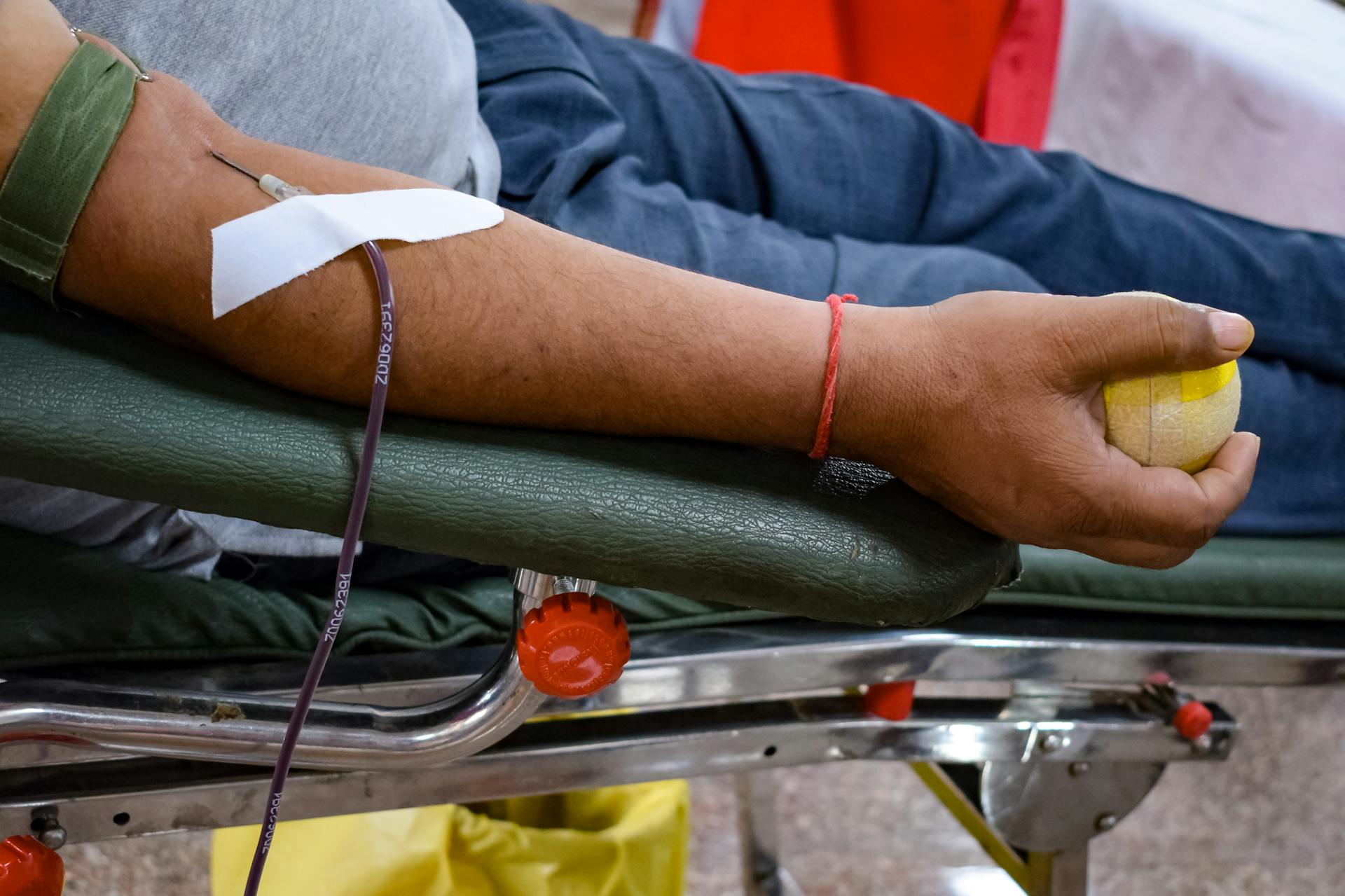 Detail view of a man's arm donating blood in a hospital environment, emphasizing healthcare support.