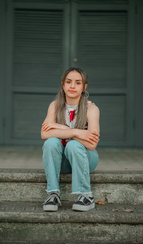 Woman in Sleeveless Shirt and Blue Denim Jeans Sitting on Concrete Stairs