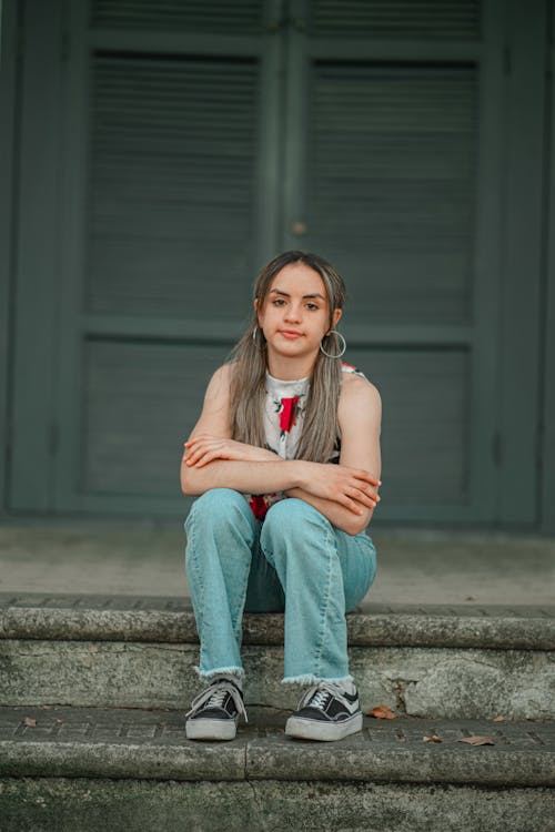 Woman in Brown Sleeveless Shirt and Blue Denim Jeans Sitting on Concrete Floor