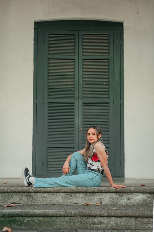 Free Fashion model sitting on steps with floral top and denim jeans, posing in front of vintage green door. Stock Photo