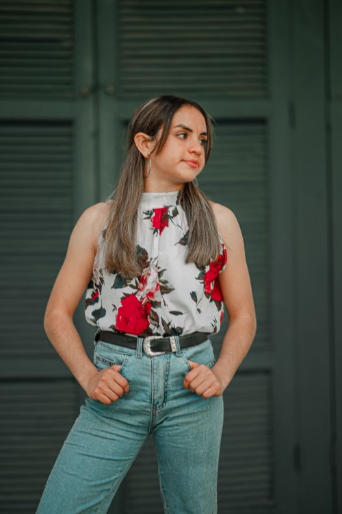 Free Young woman posing confidently in a floral top and jeans against a green background. Stock Photo