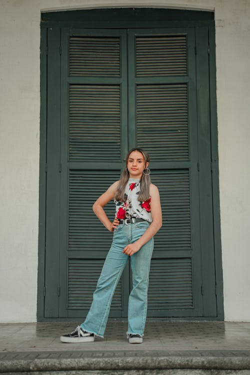 Woman in Floral Top and Denim Jeans Standing in Front of Wooden Doors