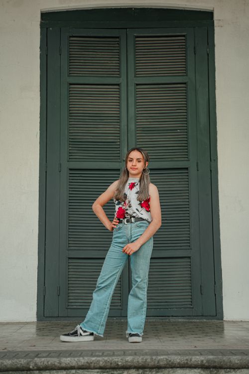Free Fashionable woman in denim jeans and floral top standing confidently by large wooden doors. Stock Photo