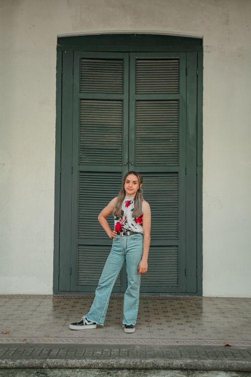 Free Stylish woman in floral top and denim poses confidently in front of large shuttered door. Stock Photo