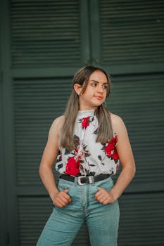 Young woman in a stylish floral top and jeans standing confidently against a shuttered background.