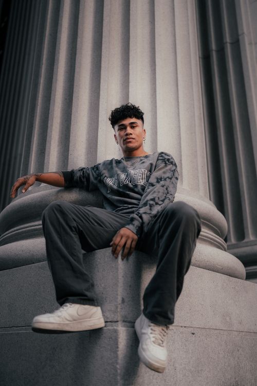 Free Young man sitting on a grand column, showcasing urban fashion style. Stock Photo