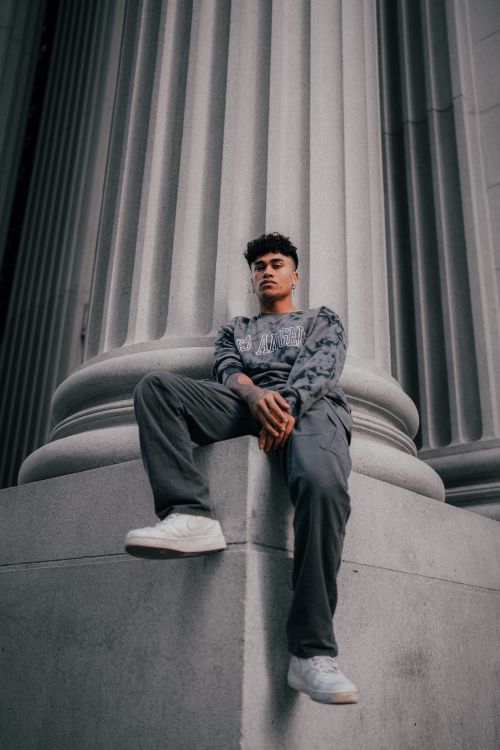 Free Young man in trendy streetwear posing against a concrete column in an urban setting. Stock Photo