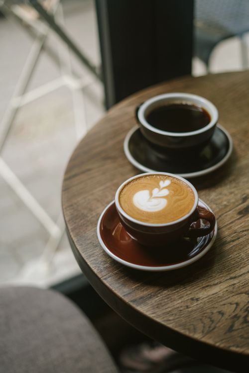 Free Warm café ambiance with latte art and espresso cups on a wooden table in daylight. Stock Photo