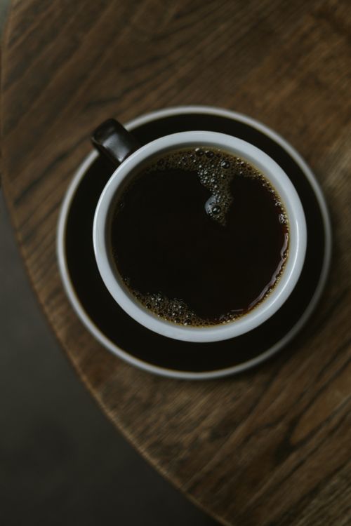 Free A steaming cup of black coffee in a black cup and saucer on a rustic wooden table. Stock Photo